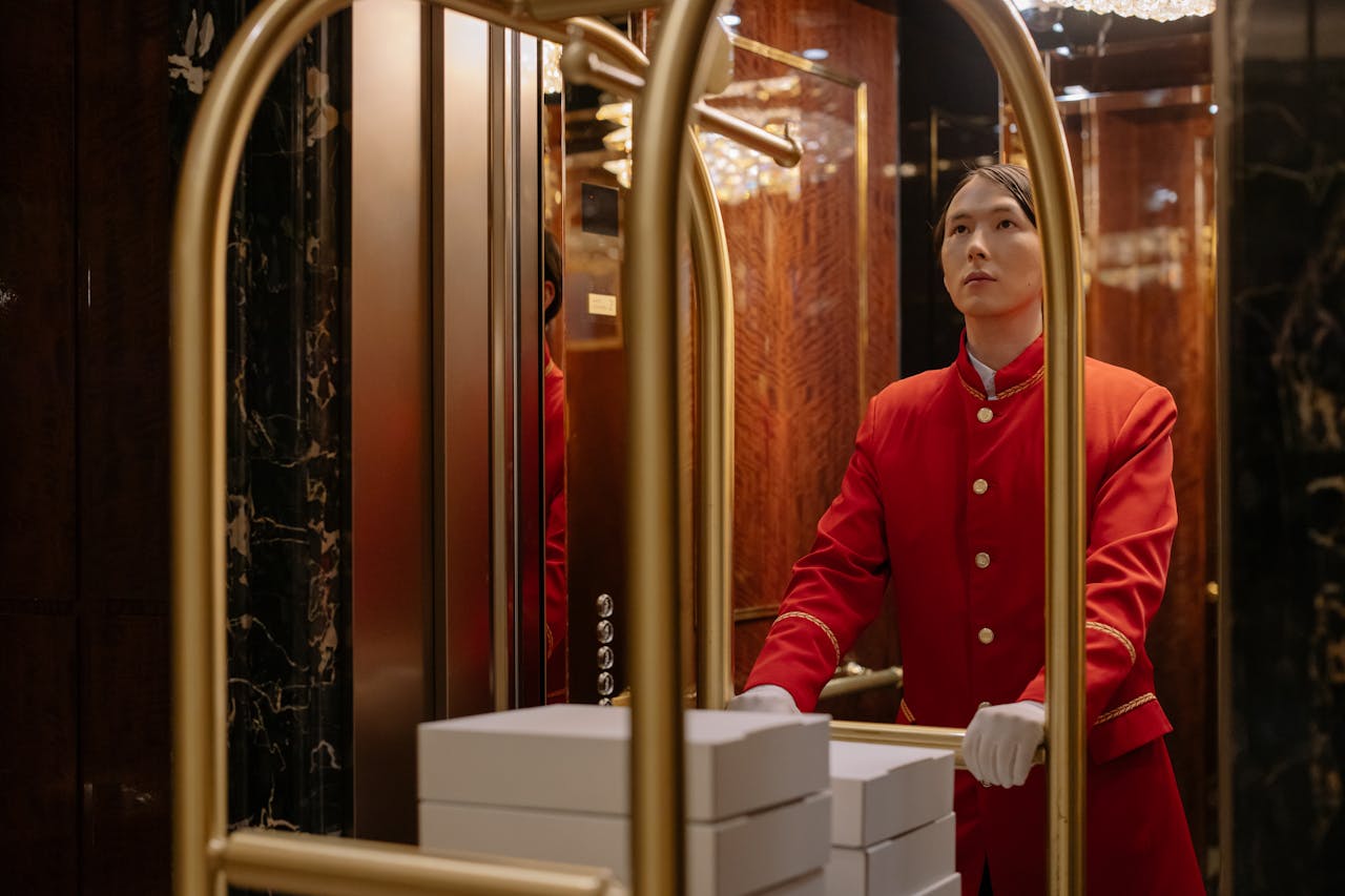 get-in-touch A hotel porter in a red uniform pushes a luggage cart in a luxurious elevator.