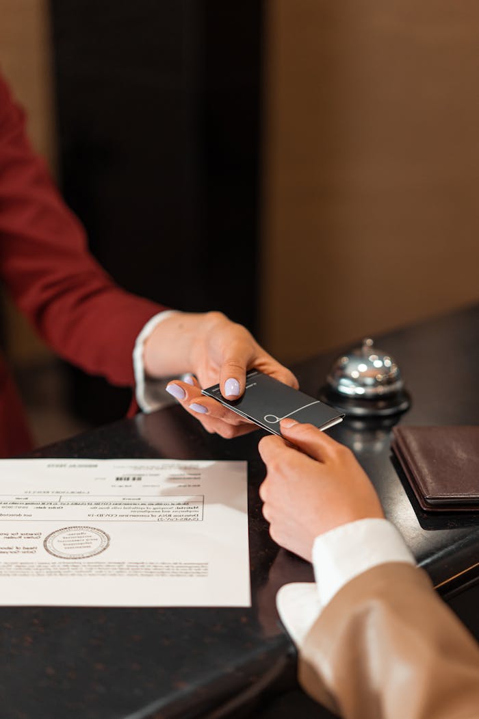 services-01 A hotel receptionist hands a key card to a guest over the counter, with documents visible.